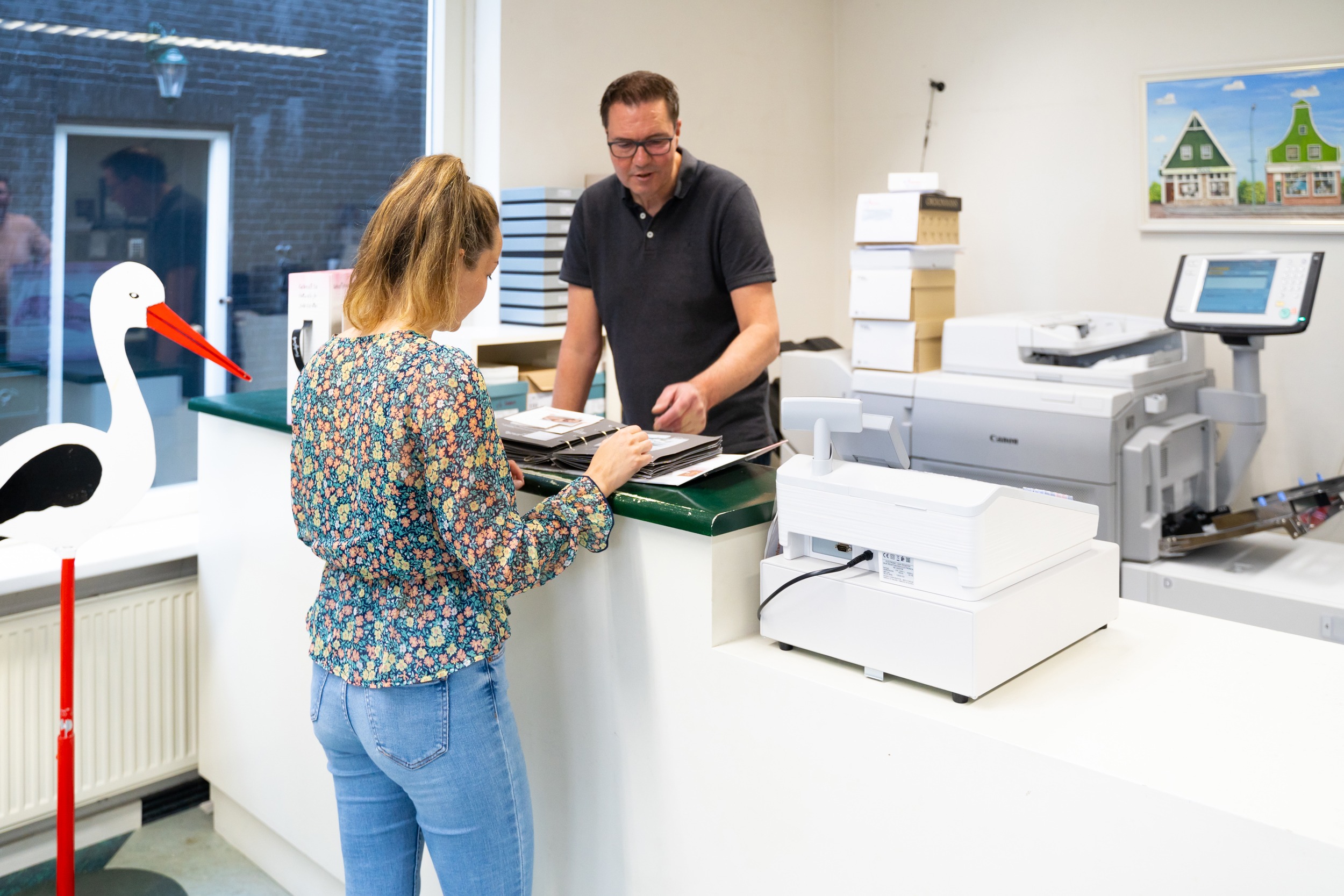 Klant achter balie in Drukkerij Zaansprint die door inspiratie boeken aan het bladeren is