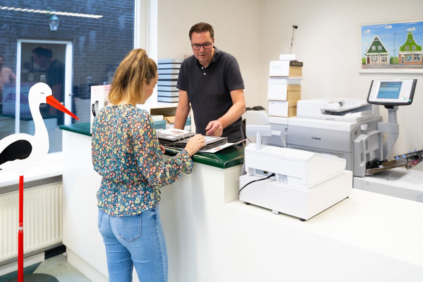 Klant achter balie in Drukkerij Zaansprint die door inspiratie boeken aan het bladeren is Klant achter balie in Drukkerij Zaansprint die door inspiratie boeken aan het bladeren is